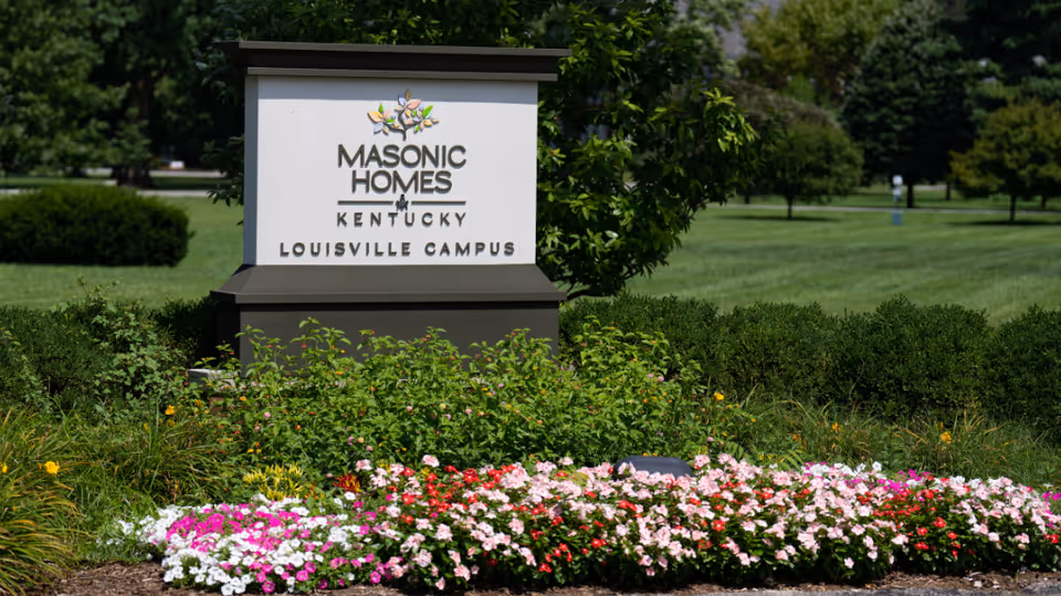 Front sign reads Masonic Homes Kentucky Louisville Campus with colorful flowers in foreground
