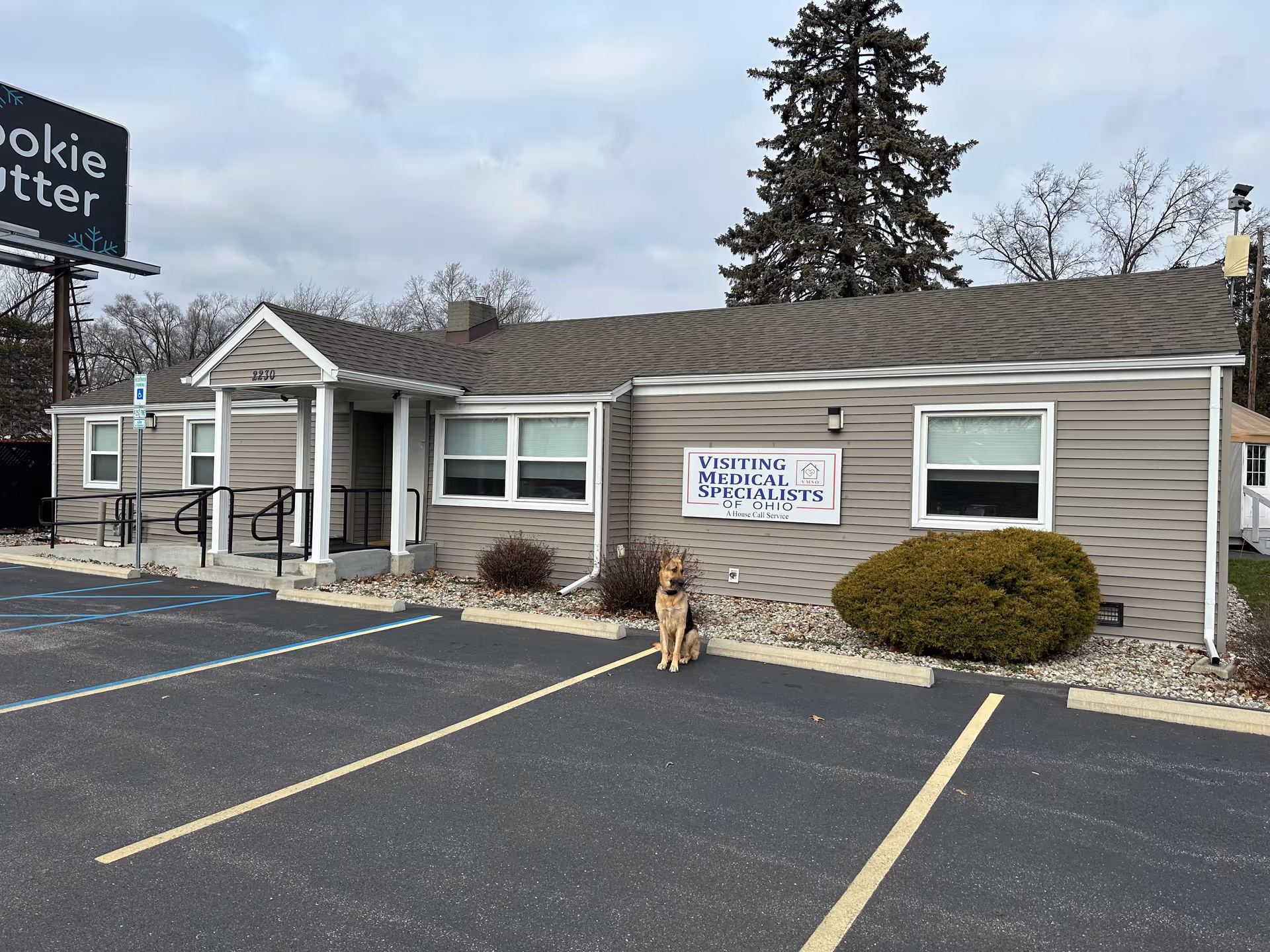 Single-story beige building with sign Visiting Medical Specialists of Ohio and a dog outside.