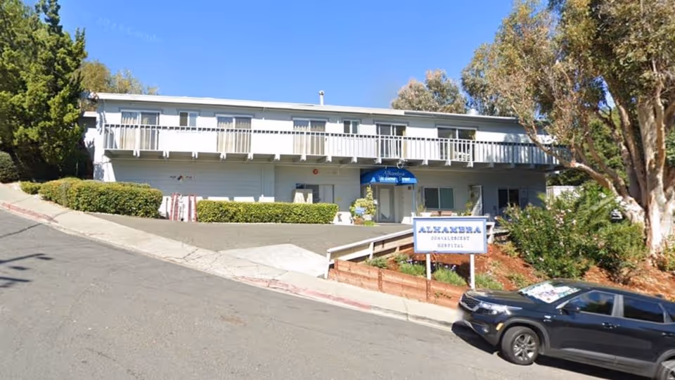 Two-story healthcare center exterior with ramp, sign, and a parked car.