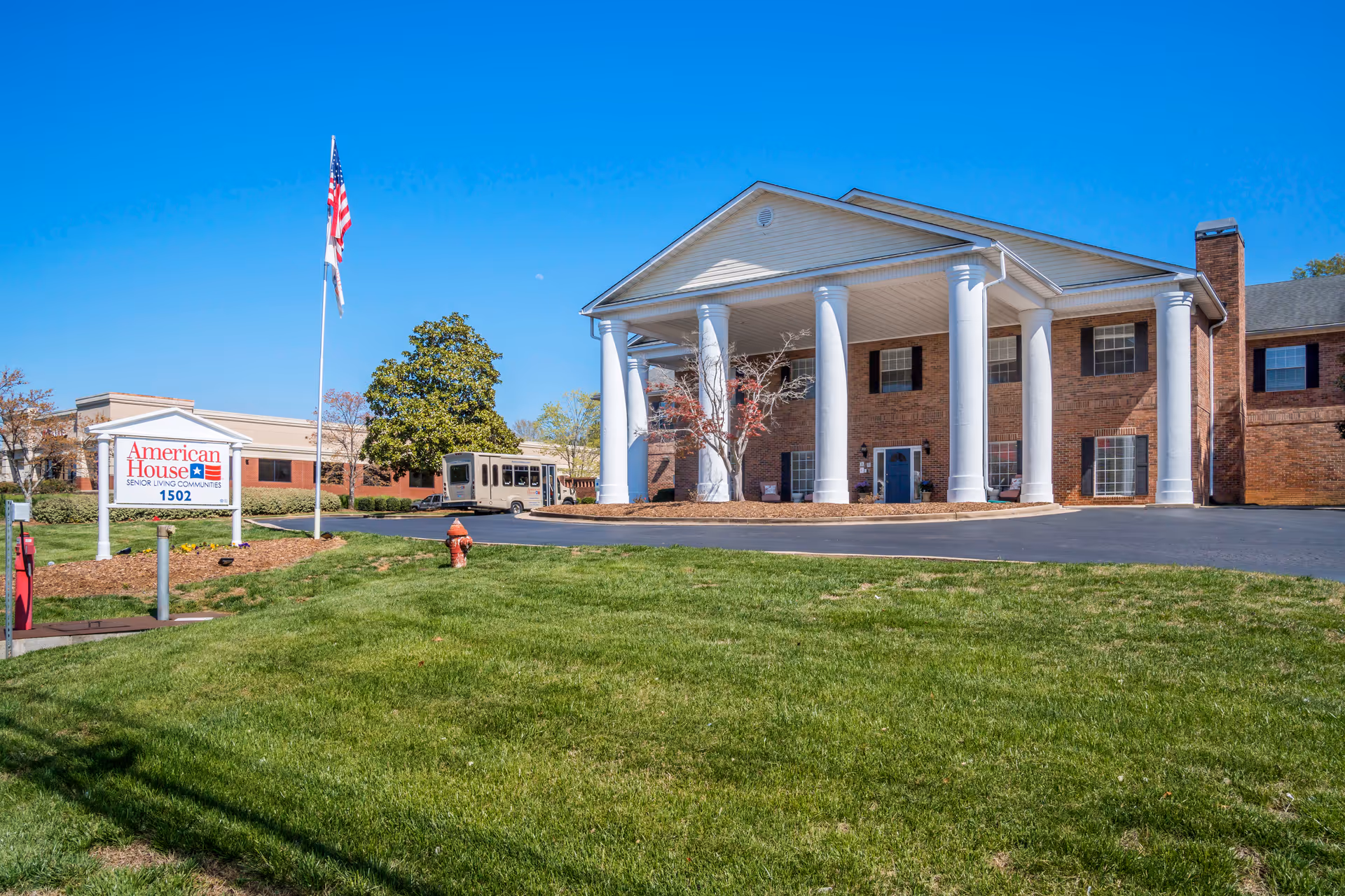 American House Hamilton Place exterior featuring brick building, four white columns, flag, and a green lawn.