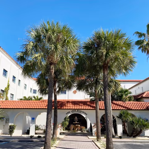 White stucco building with red-tiled roof, arches, and palm trees at the entrance.
