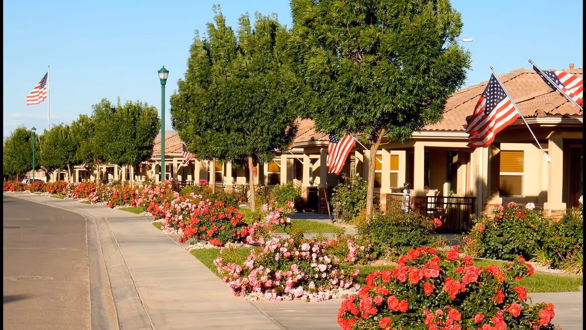Row of single-story homes with red-tiled roofs, flags, and rose-lined walkways.