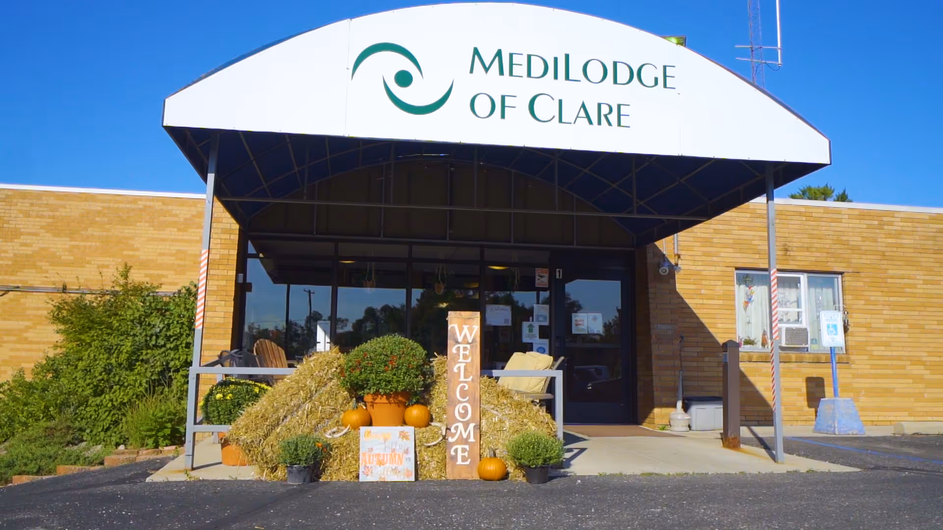 Front entrance of Medilodge of Clare with autumn decorations and welcome sign.