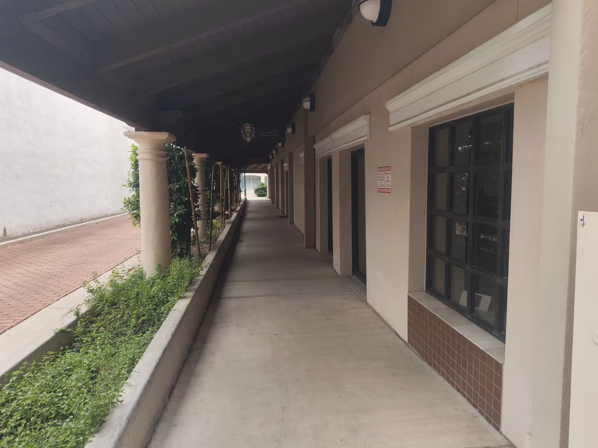 Covered exterior corridor of a senior facility with columns, windows, and greenery.
