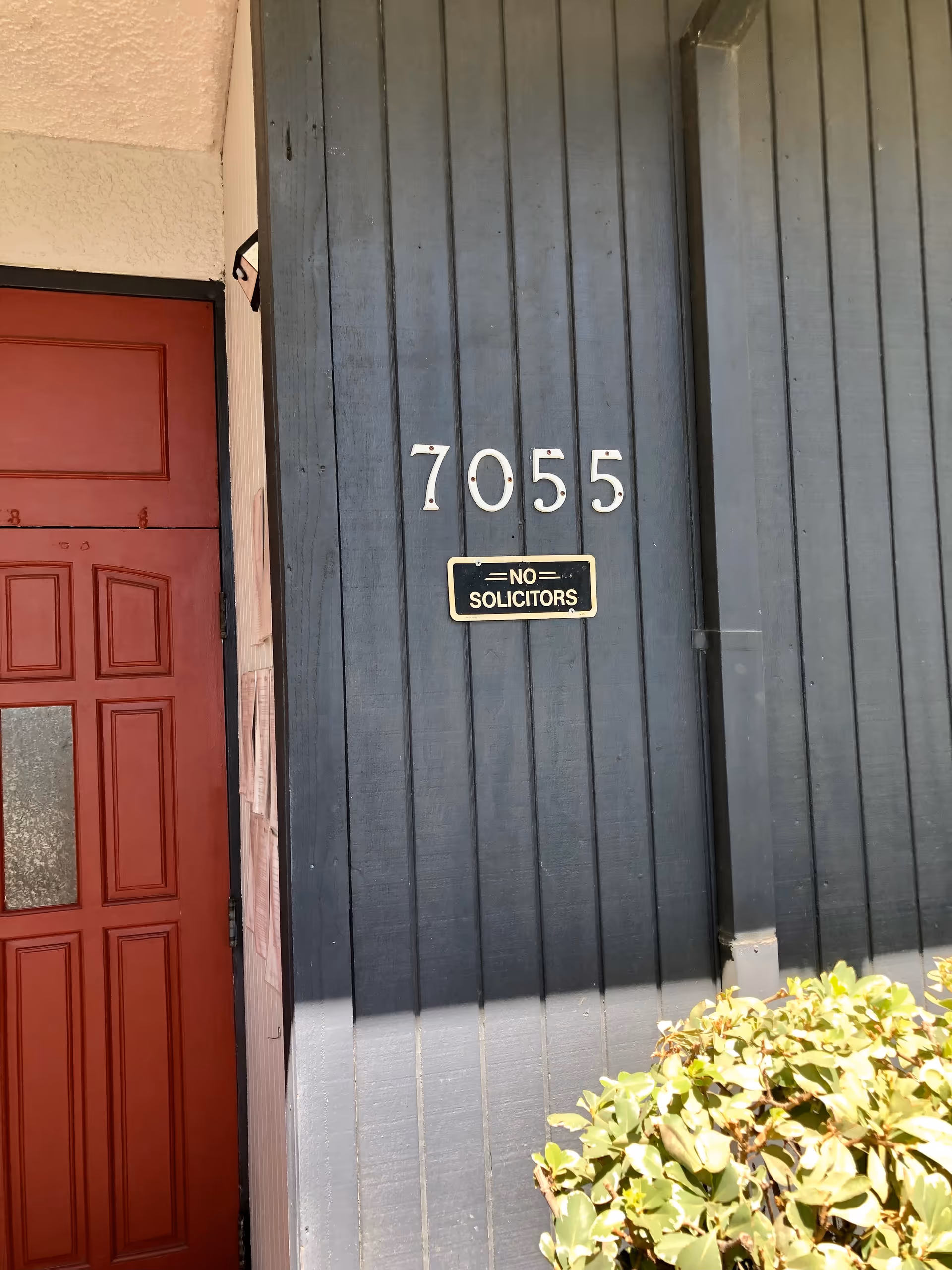Dark blue exterior wall with address 7055, red door on left, No Solicitors sign.