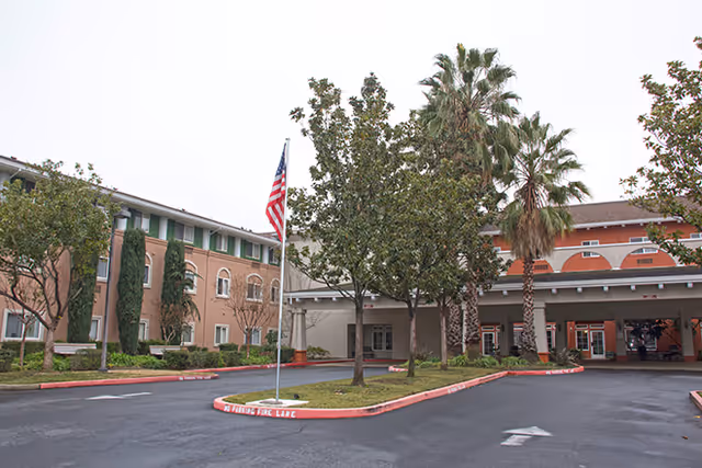 Exterior view of Cogir of Stock Ranch, with palm trees, flag, and covered entrance.