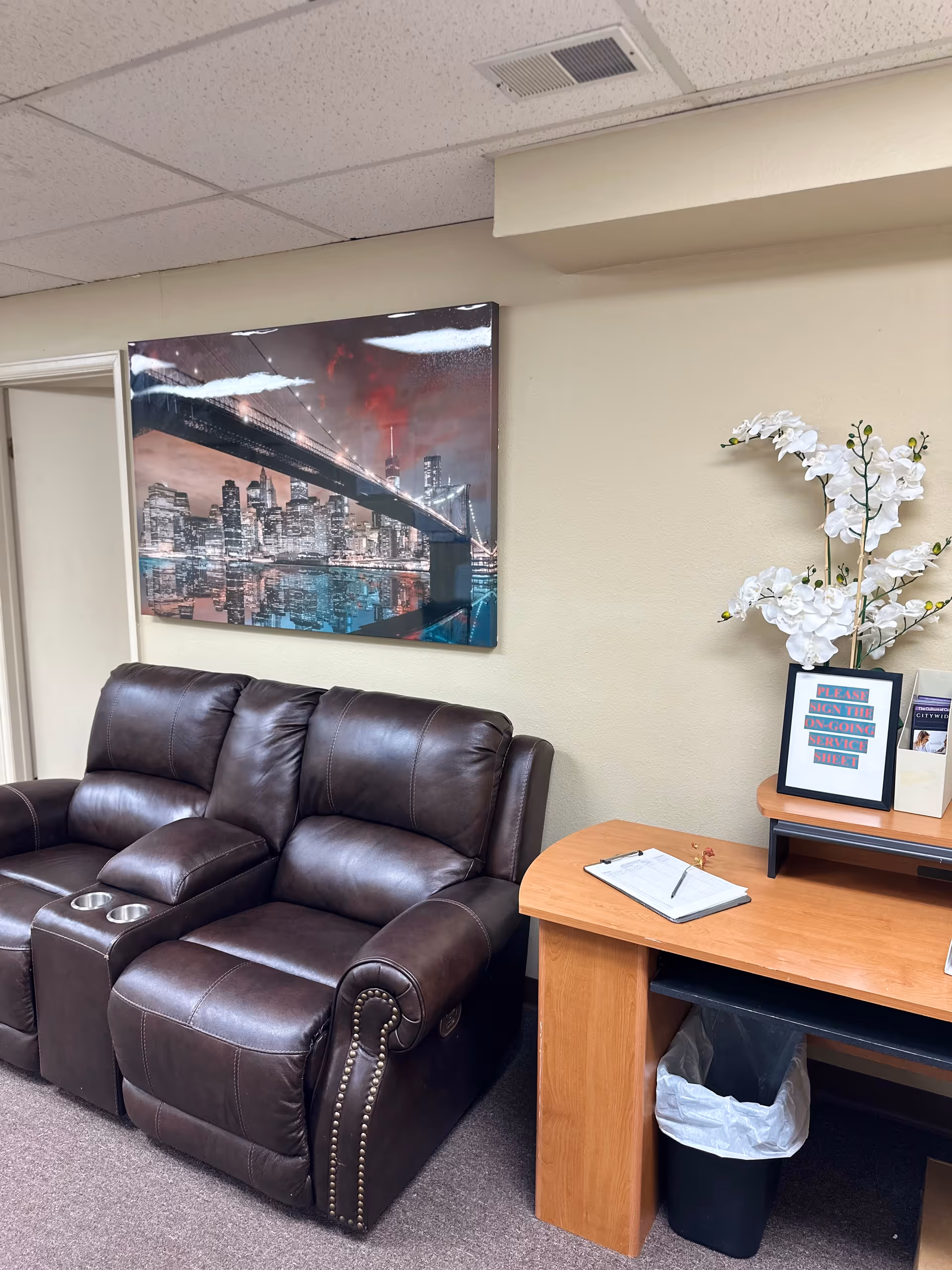 A dark brown leather sofa in a reception area with a desk and wall art.