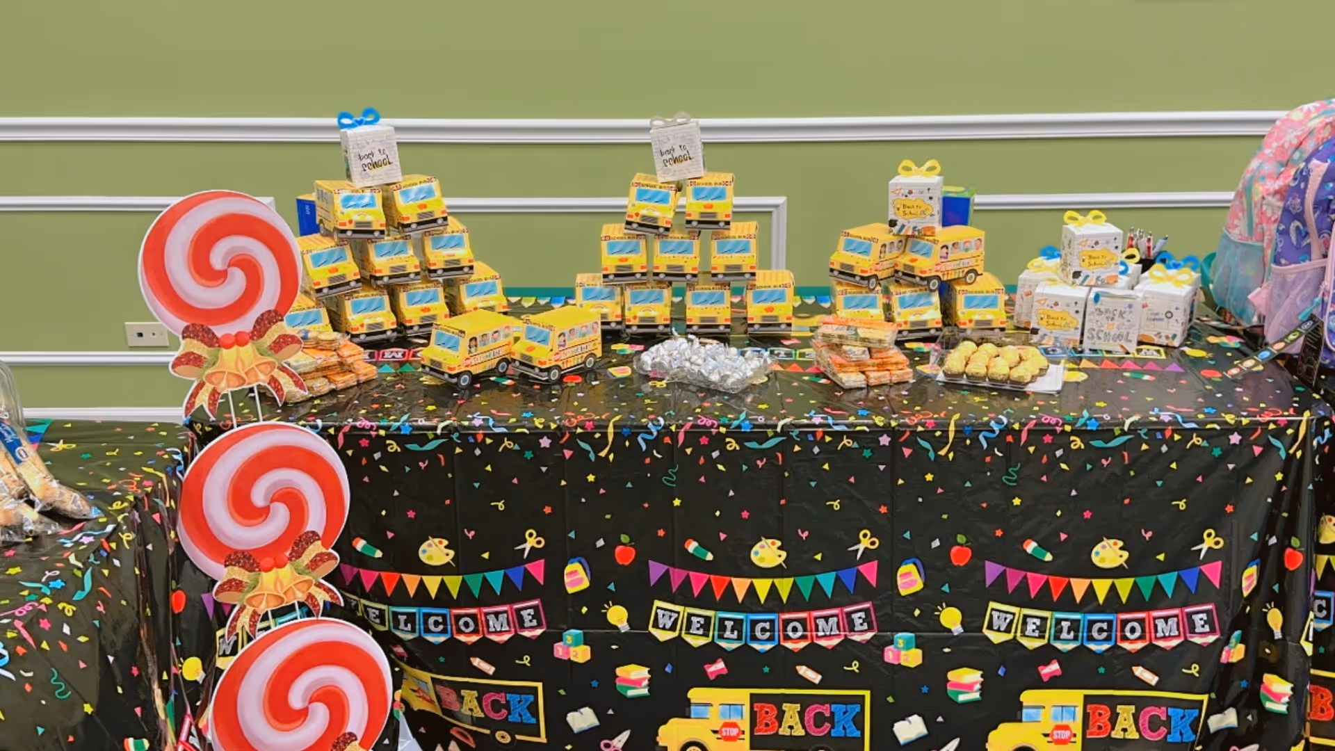 Decorated table with toy buses, lollipops, gifts, and colorful banners in a celebratory setup.