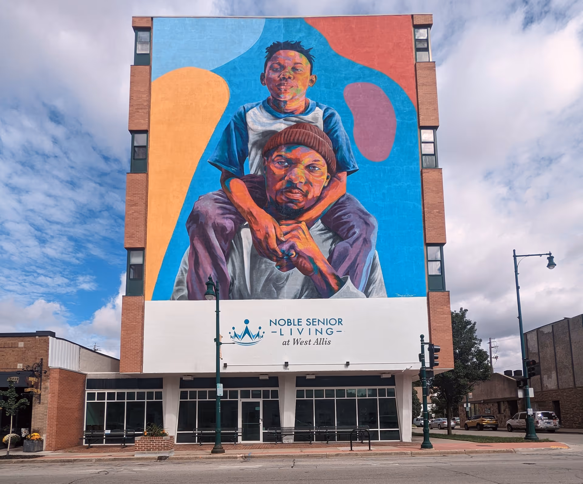 Tall brick building with a large colorful mural depicting two people and Noble Senior Living signage.