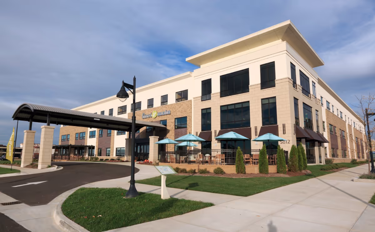 Exterior view of American House Wyoming facility with brick facade, walkway, and outdoor seating.