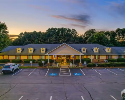 Front view of a single-story senior living building with a parking lot and marked handicap spaces at sunset.