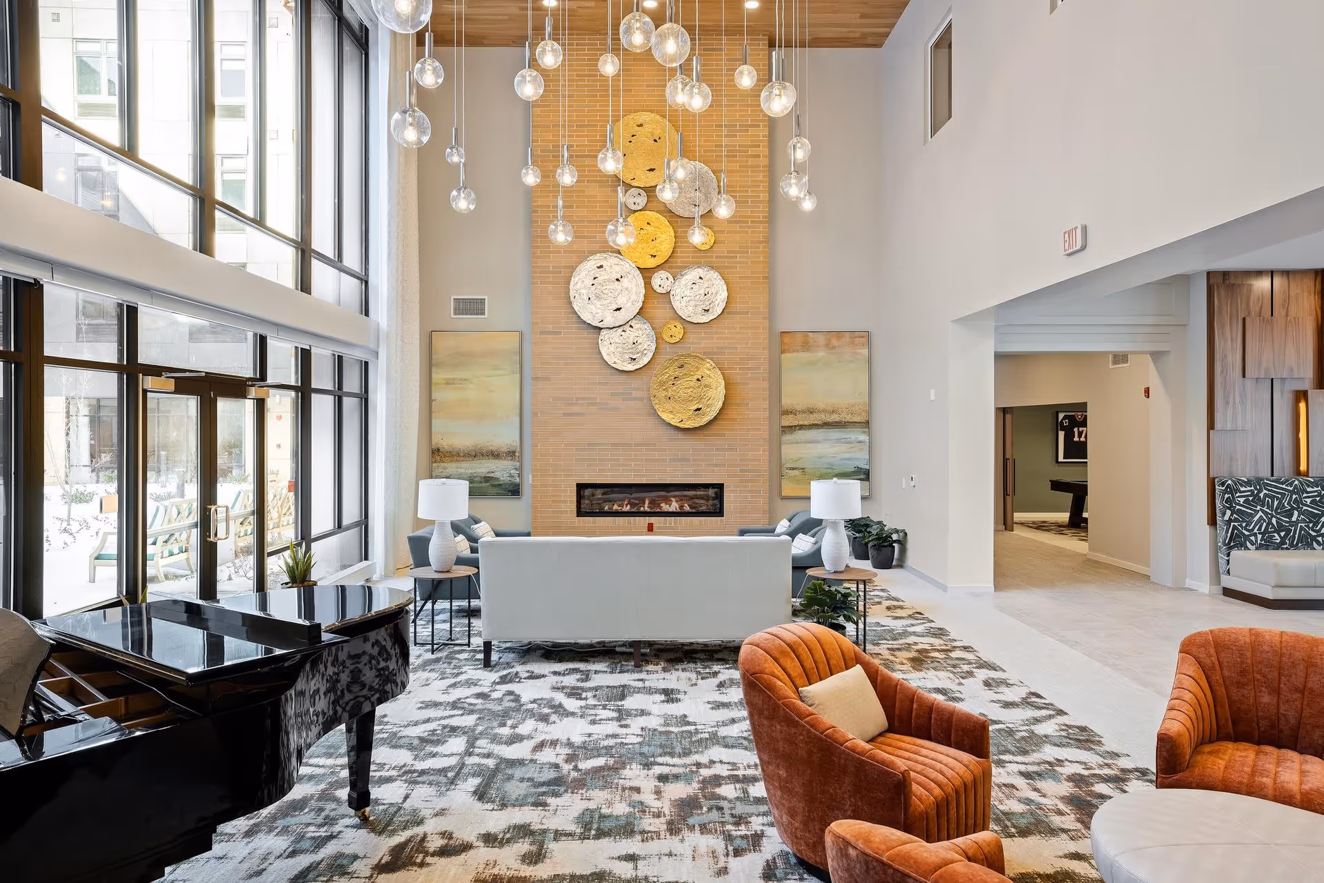 Bright, modern lounge with a grand piano, seating area, fireplace, and hanging pendant lights.