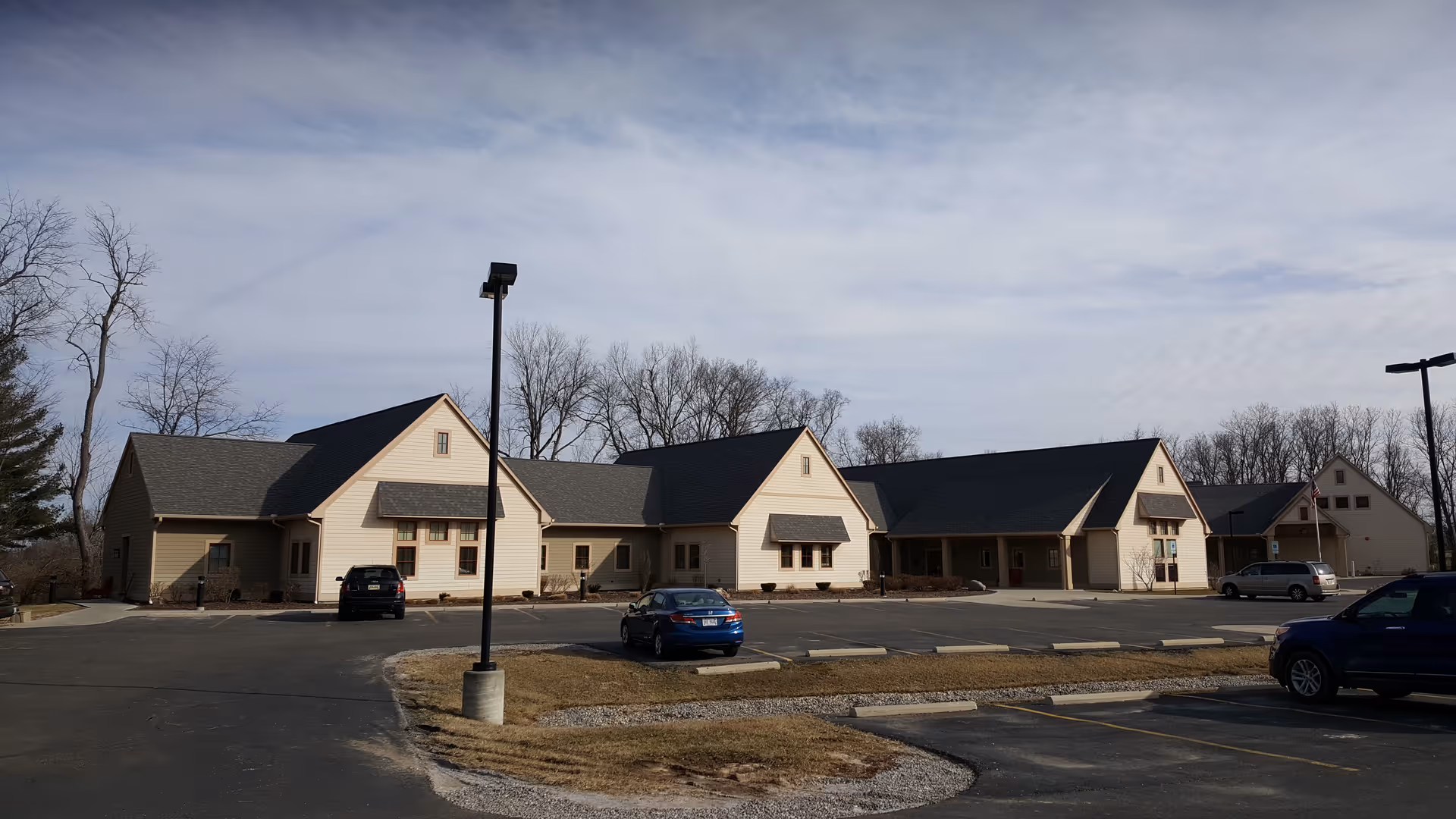 Exterior view of a beige, multi-wing senior living facility with a parking lot.