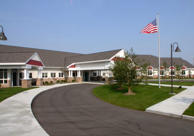 Exterior view of Sterling Senior Community V, curved driveway, flagpole, and landscaped front lawn.