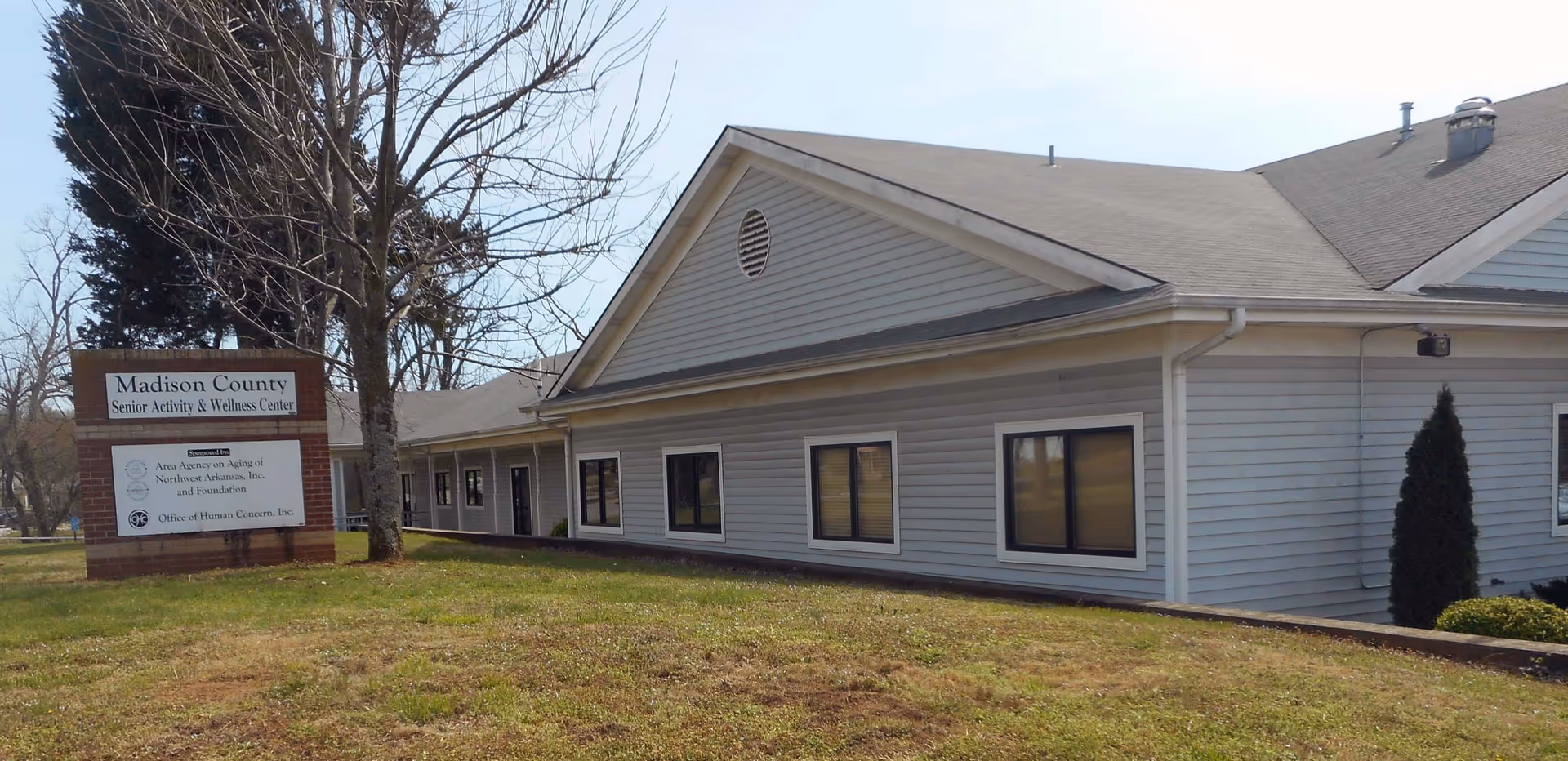 Exterior view of a single-story senior activity center with a sign and lawn.