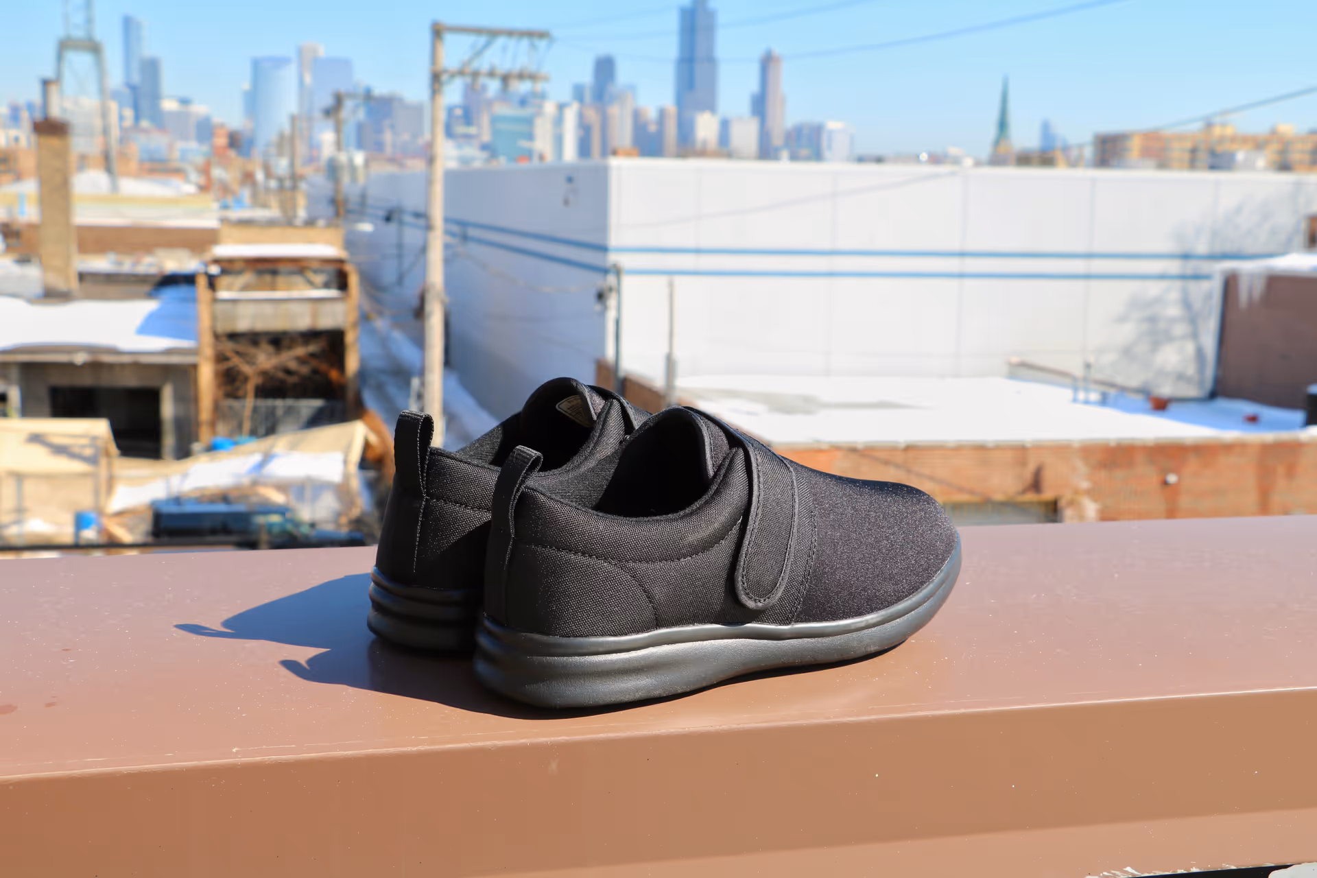 A pair of black athletic shoes rests on a brown railing with a city skyline behind.