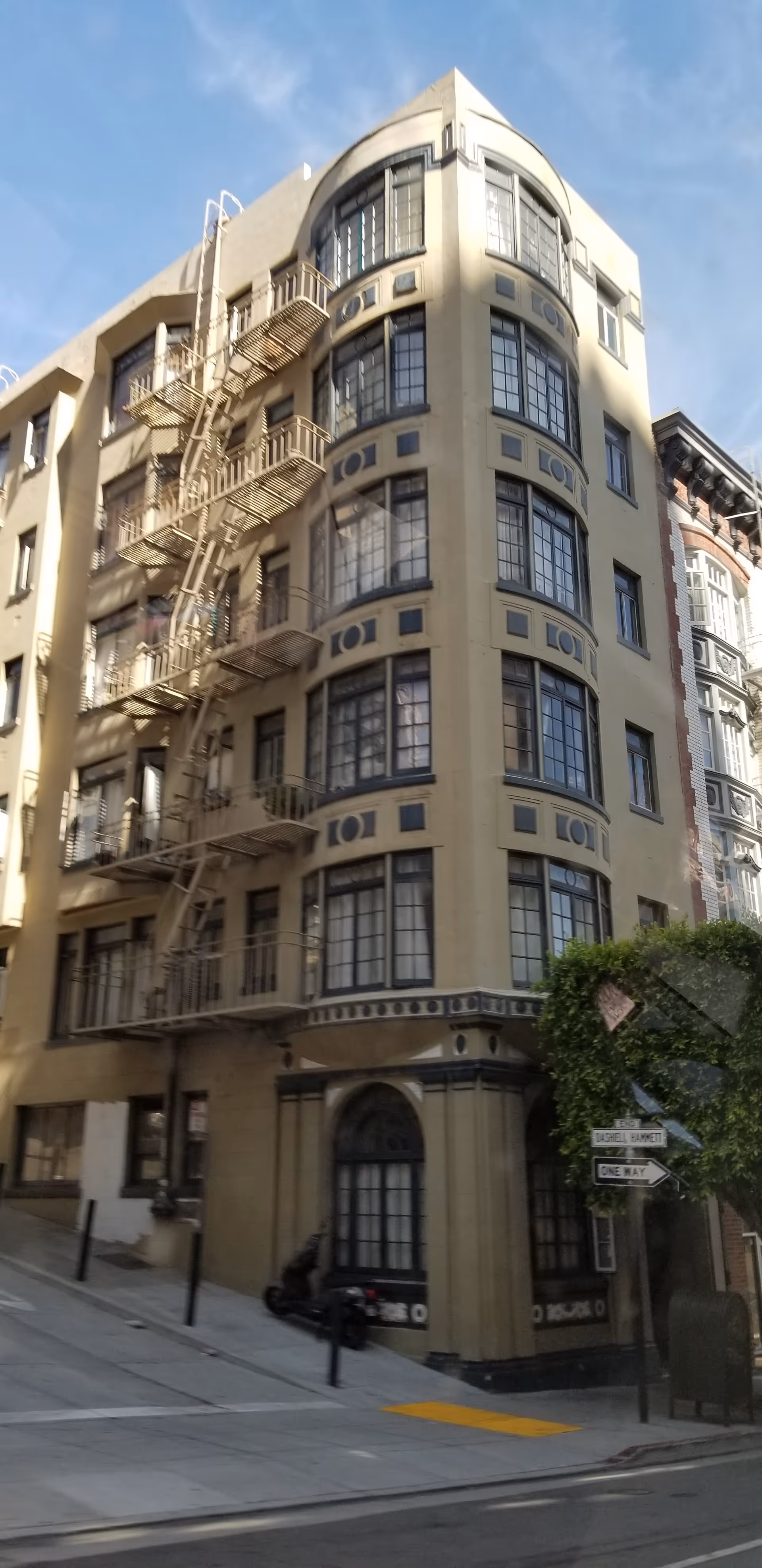 Tall beige building with exterior fire escapes on a curved corner, under blue sky.