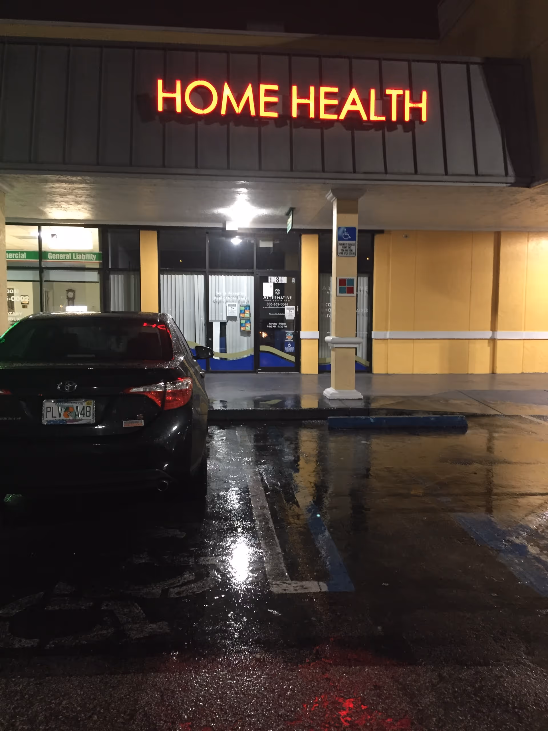 Night exterior of a facility with a bright red HOME HEALTH sign and a parked car.