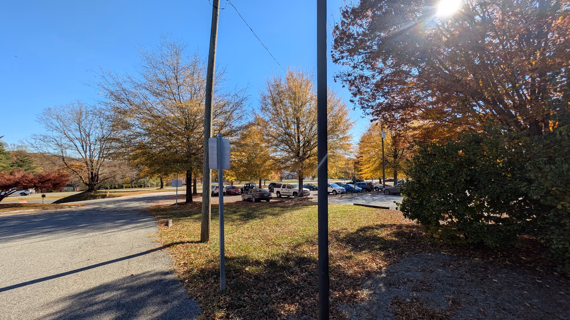 Sunny outdoor parking area at a senior living campus with trees and a bench.