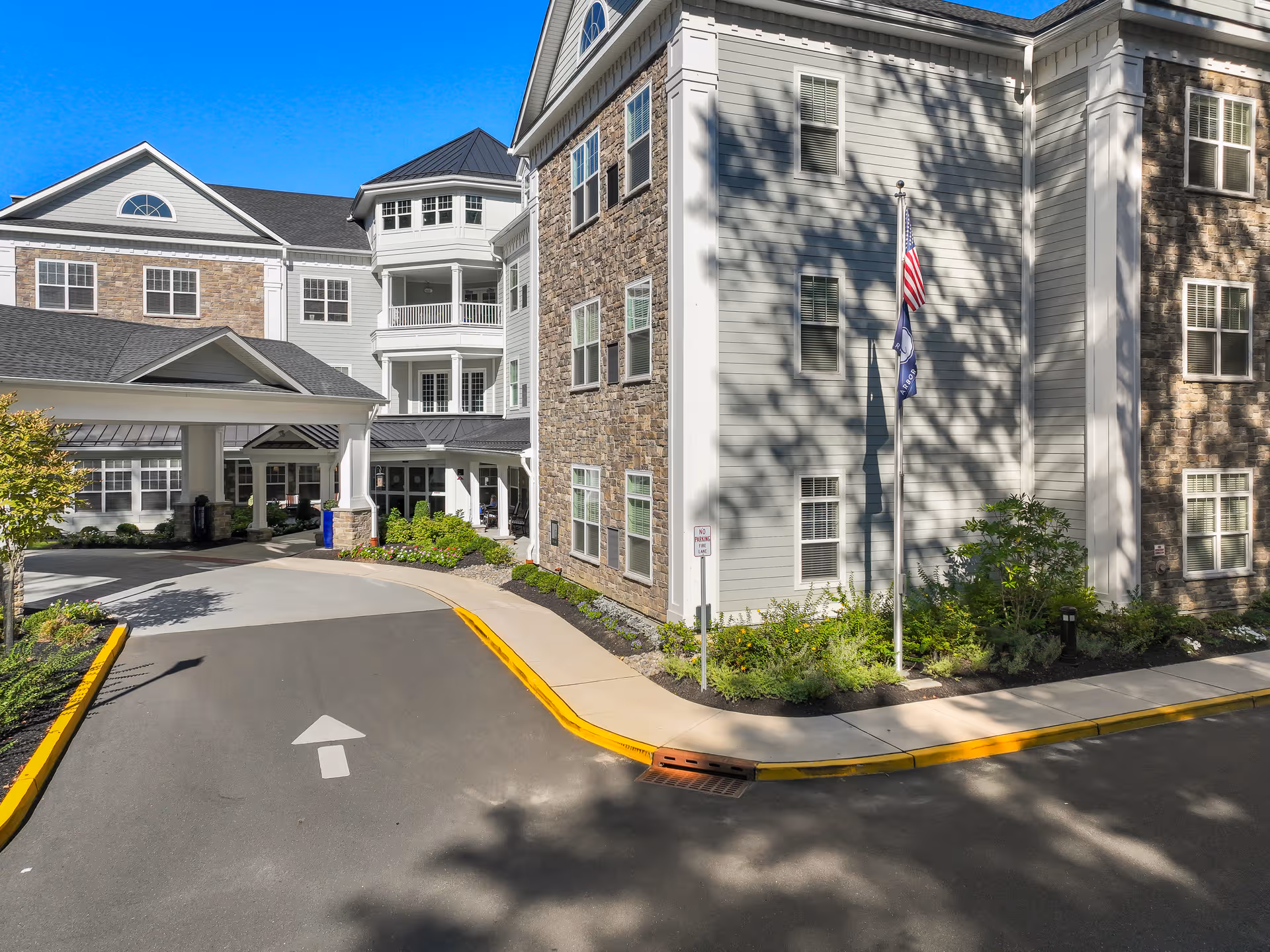 Exterior view of Arbor Terrace Marlton with driveway, entrance, and flag near the building.