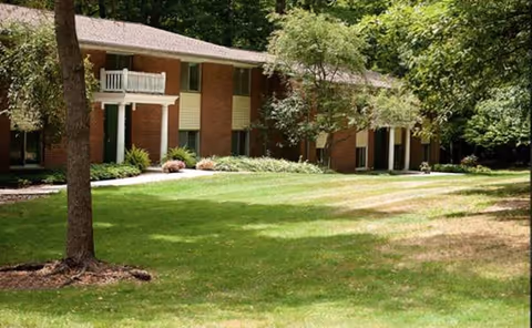 Red brick senior living facility exterior with balconies and a well-kept green lawn.