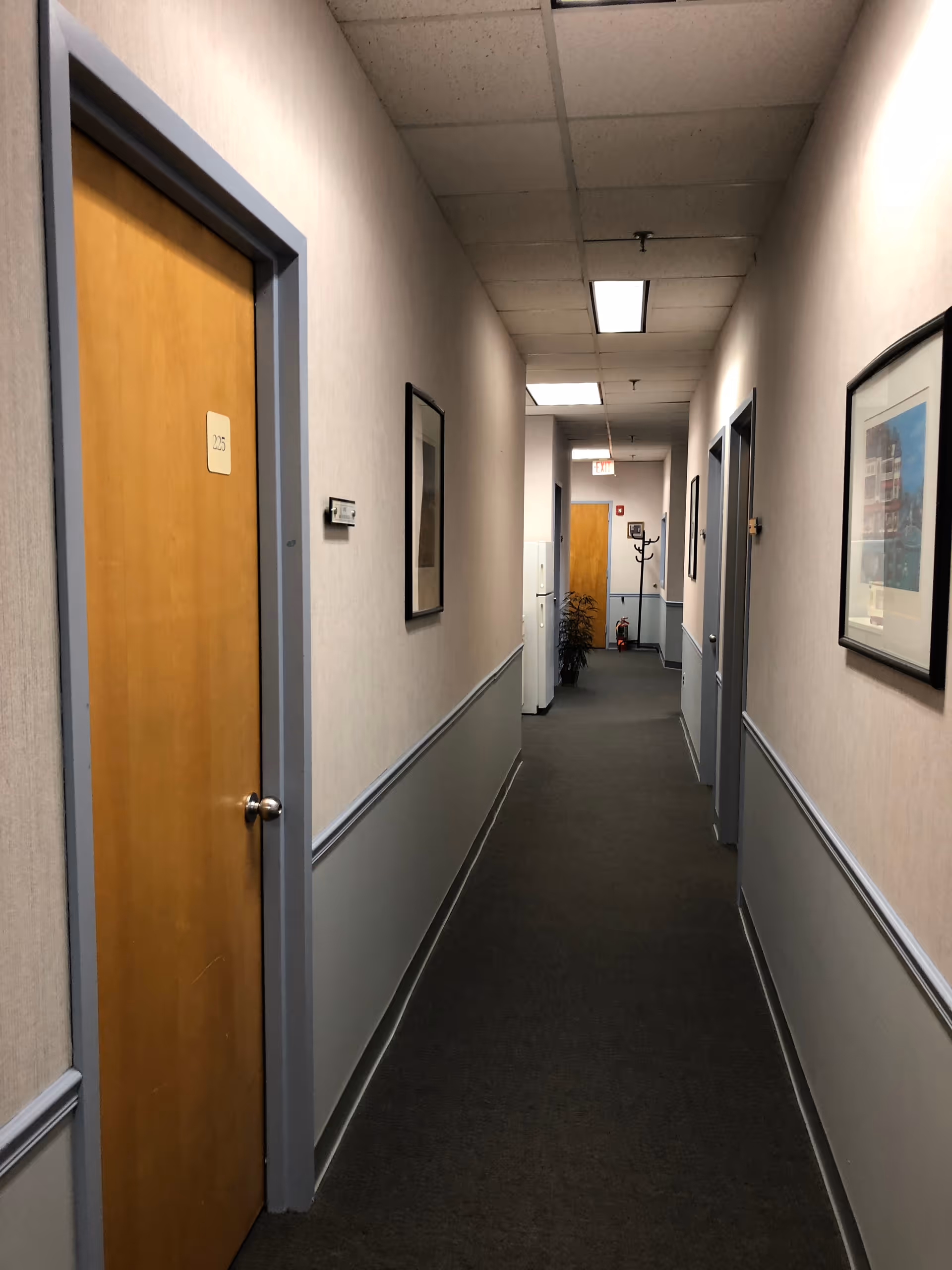 Long indoor hallway with closed doors, framed pictures, and neutral walls in a senior facility.