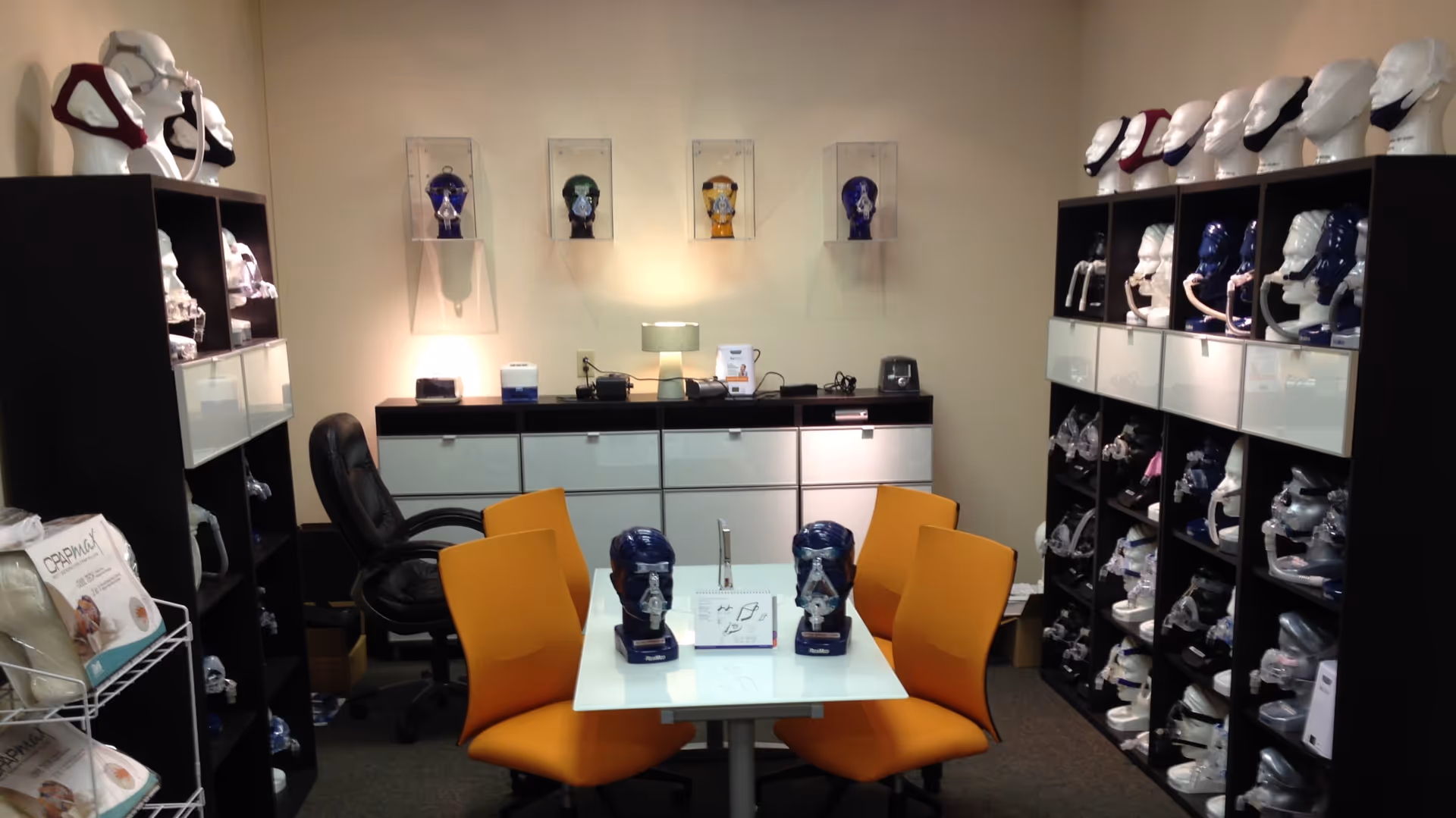 Interior showroom with orange chairs around a glass table, prosthetic display shelves.