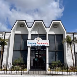 White modern building entrance with a sign reading Downey Community Health Center and palm trees.