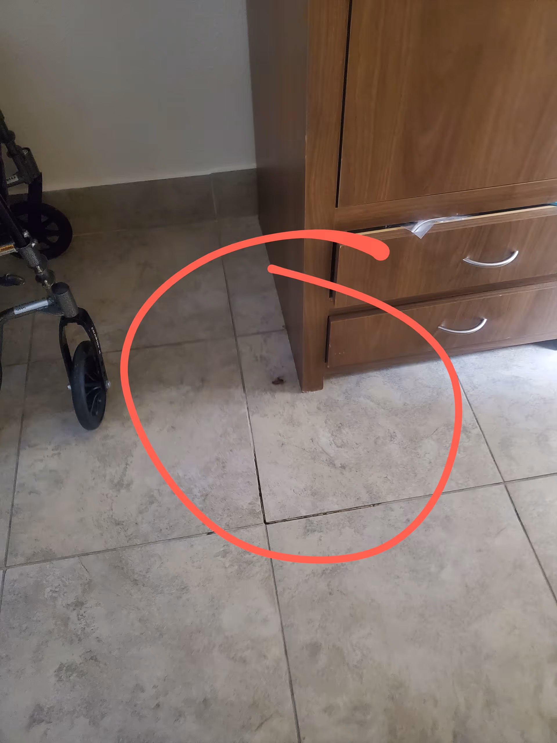 Wheelchair beside a wooden cabinet in a hallway, showing cracked floor tile.