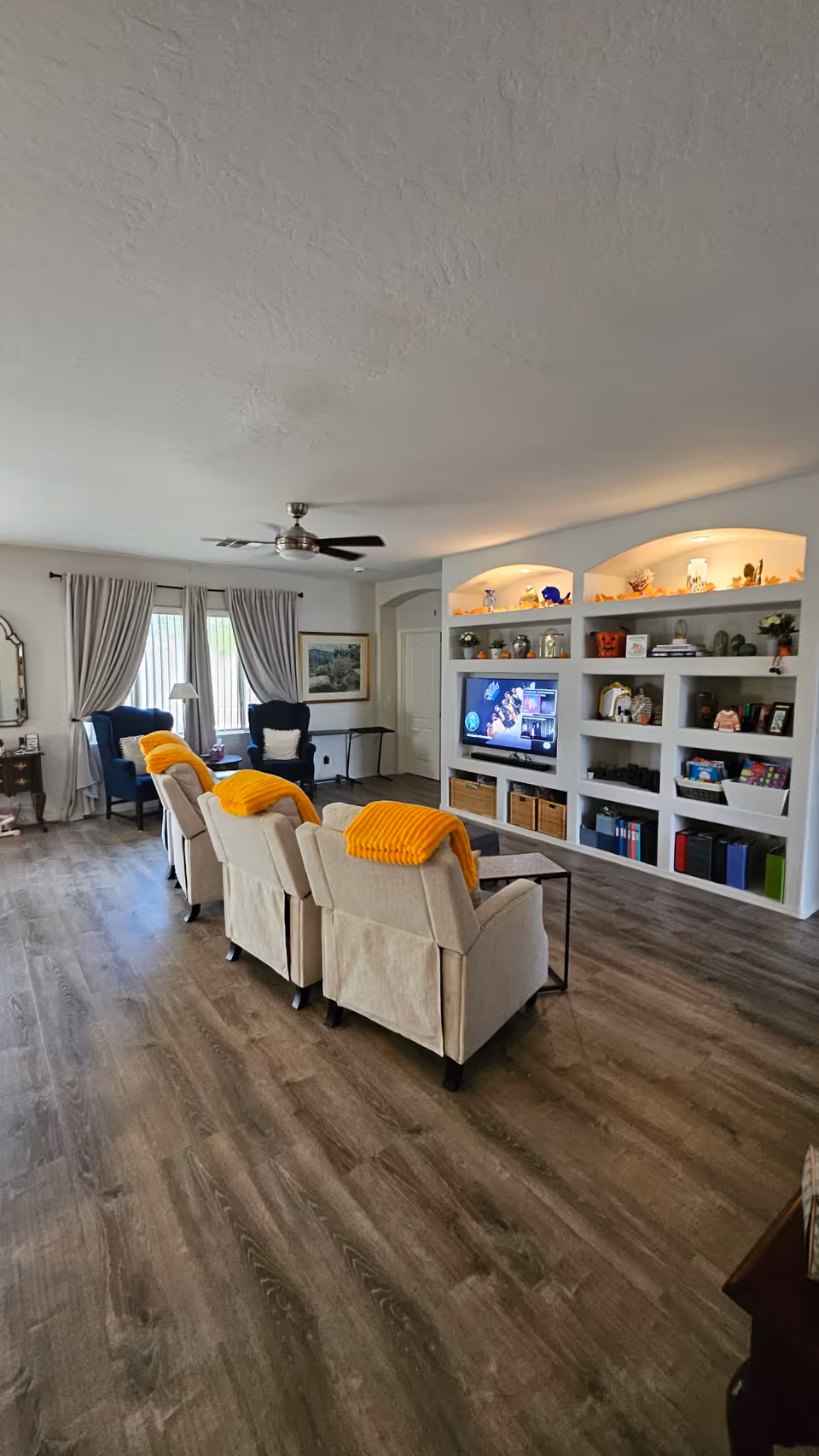 Bright living room with beige recliners, a TV in built-in shelves, and wood floors.