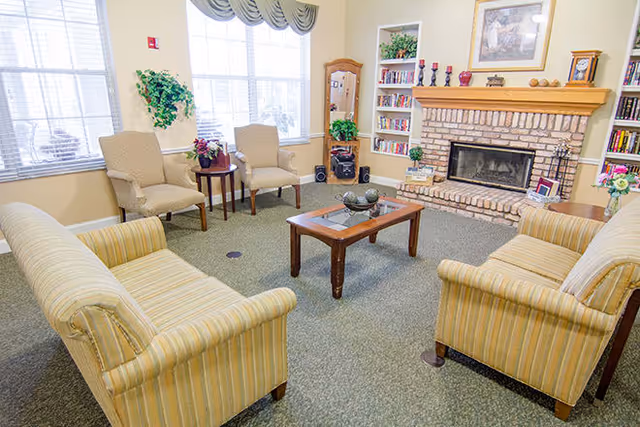 Communal living room with striped sofas, armchairs, a coffee table, bookshelves and a brick fireplace.