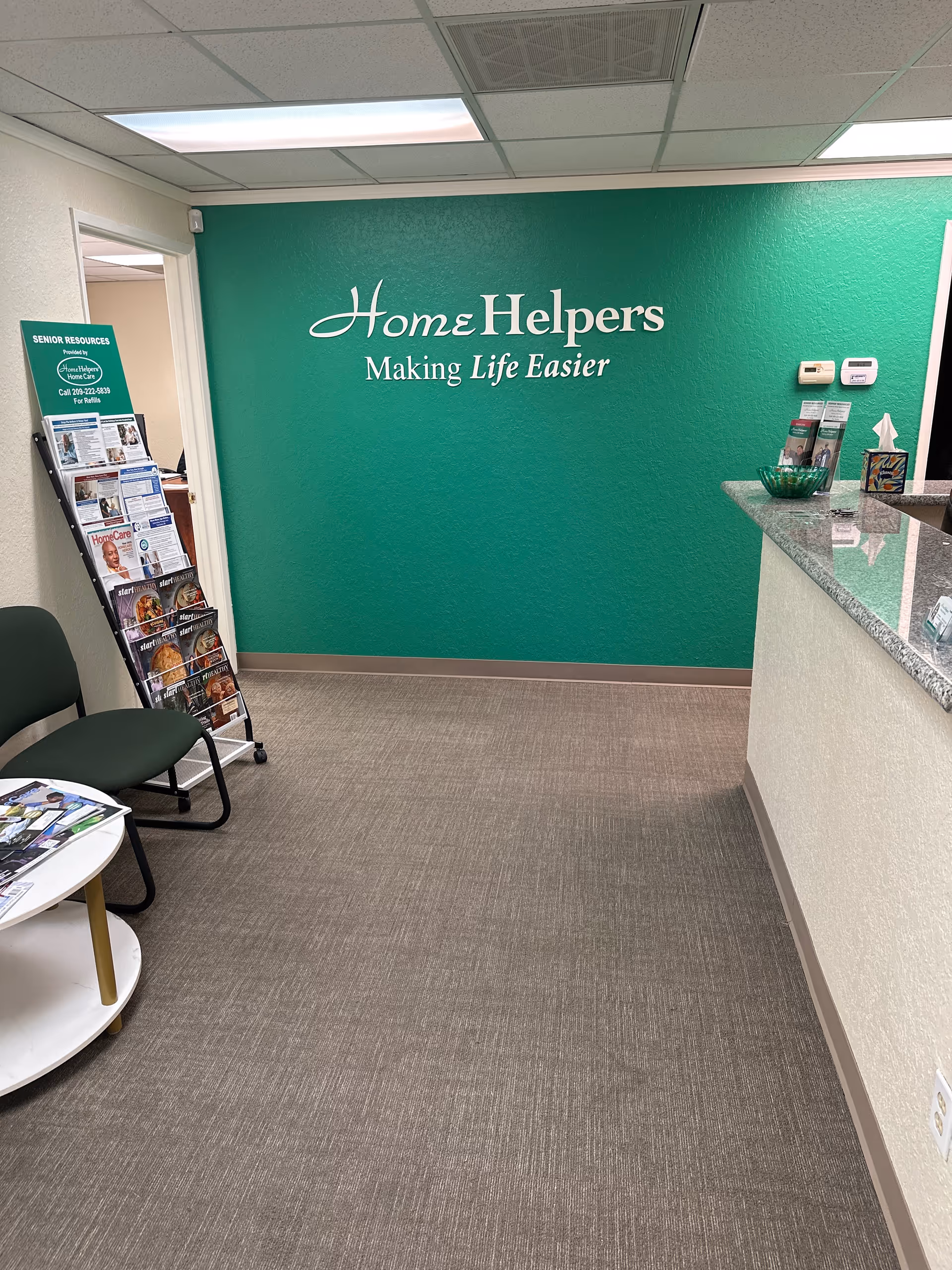 Reception area with green branded wall and brochure rack at Home Helpers office