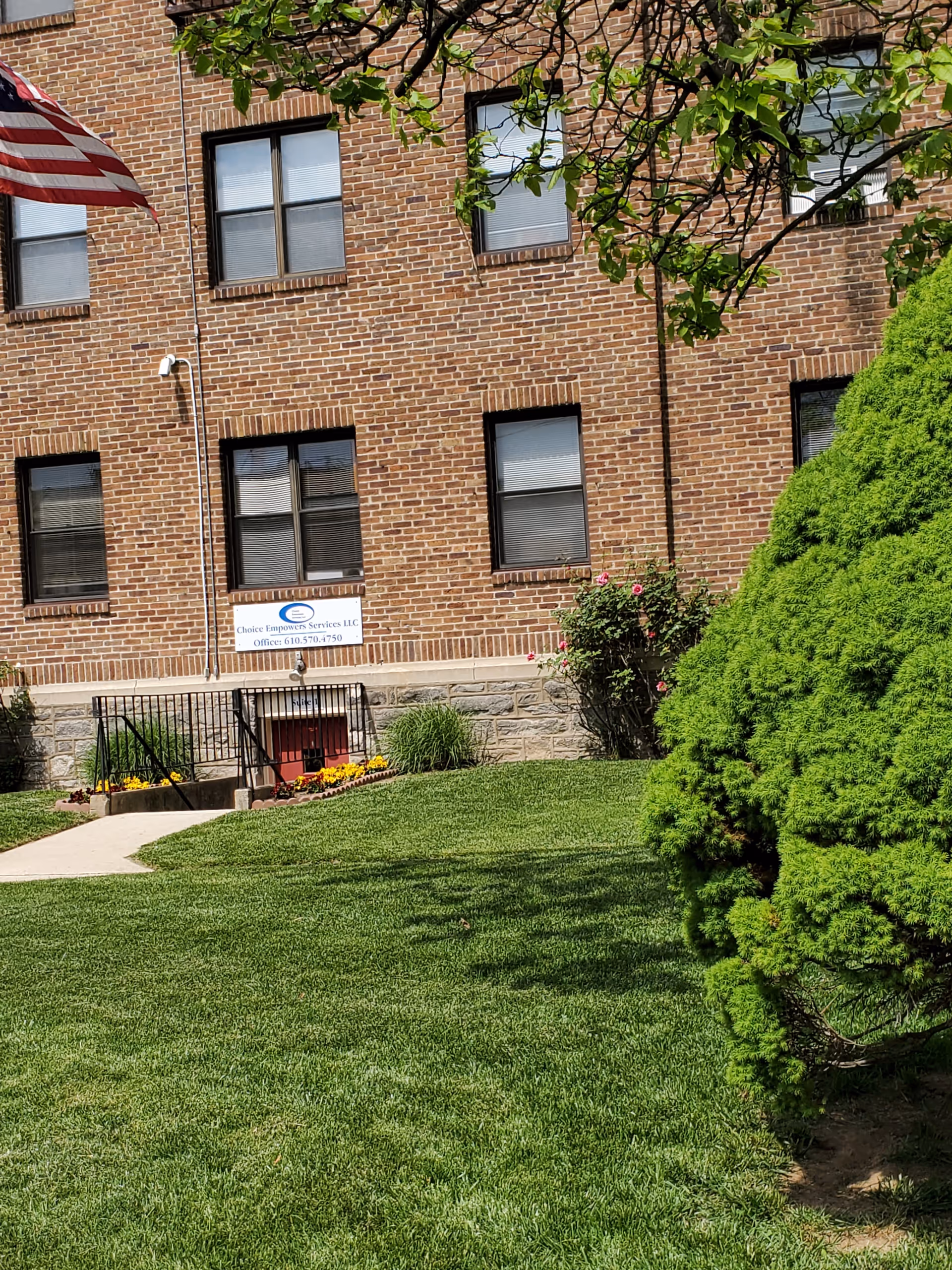 Brick building exterior with a sign, American flag, and a well-kept green lawn