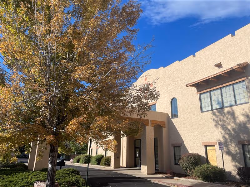 Front exterior of a beige senior living facility with a covered entrance and autumn tree.