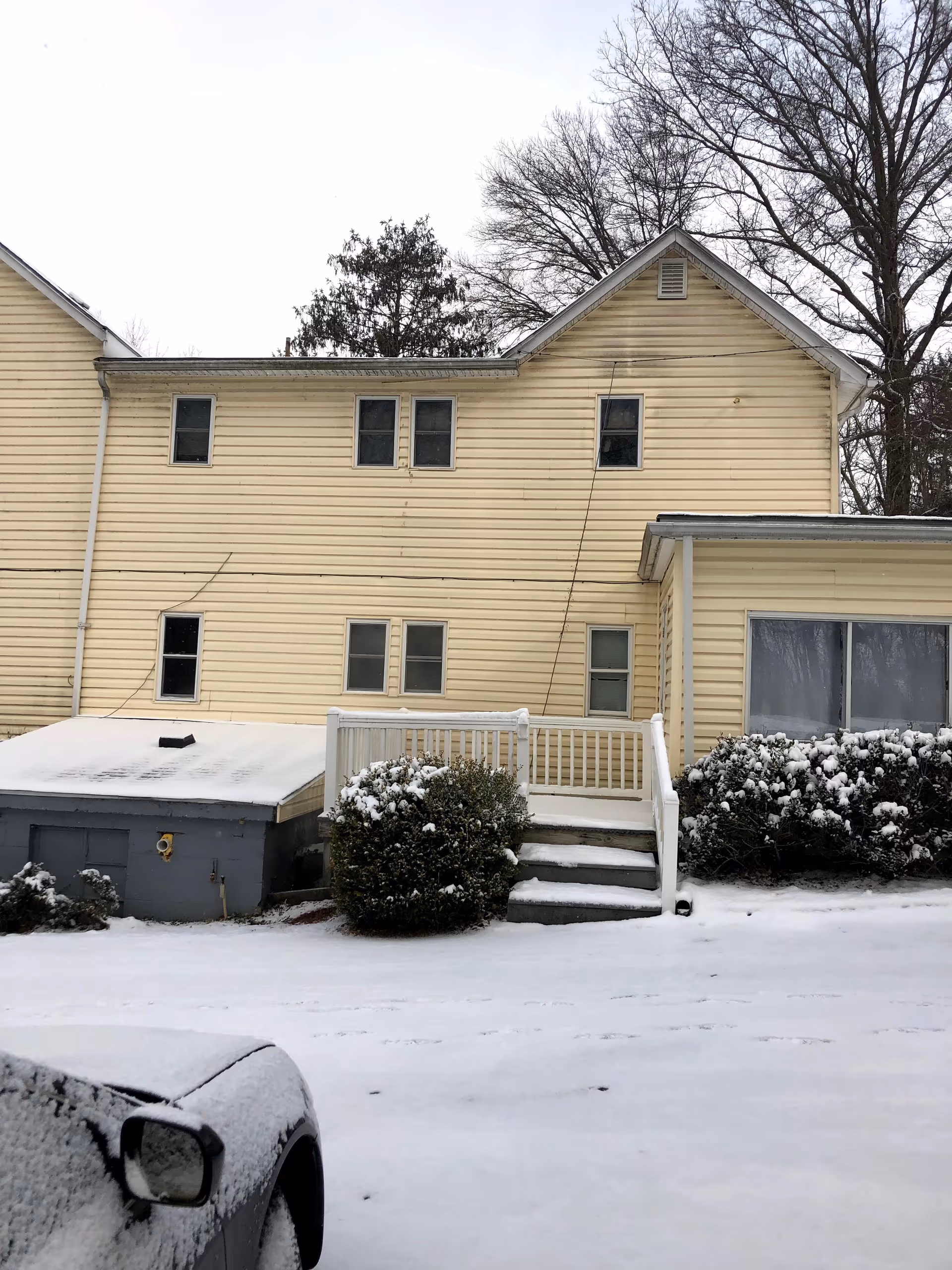 Yellow two-story assisted living building exterior with snow, stairs, and shrubs.