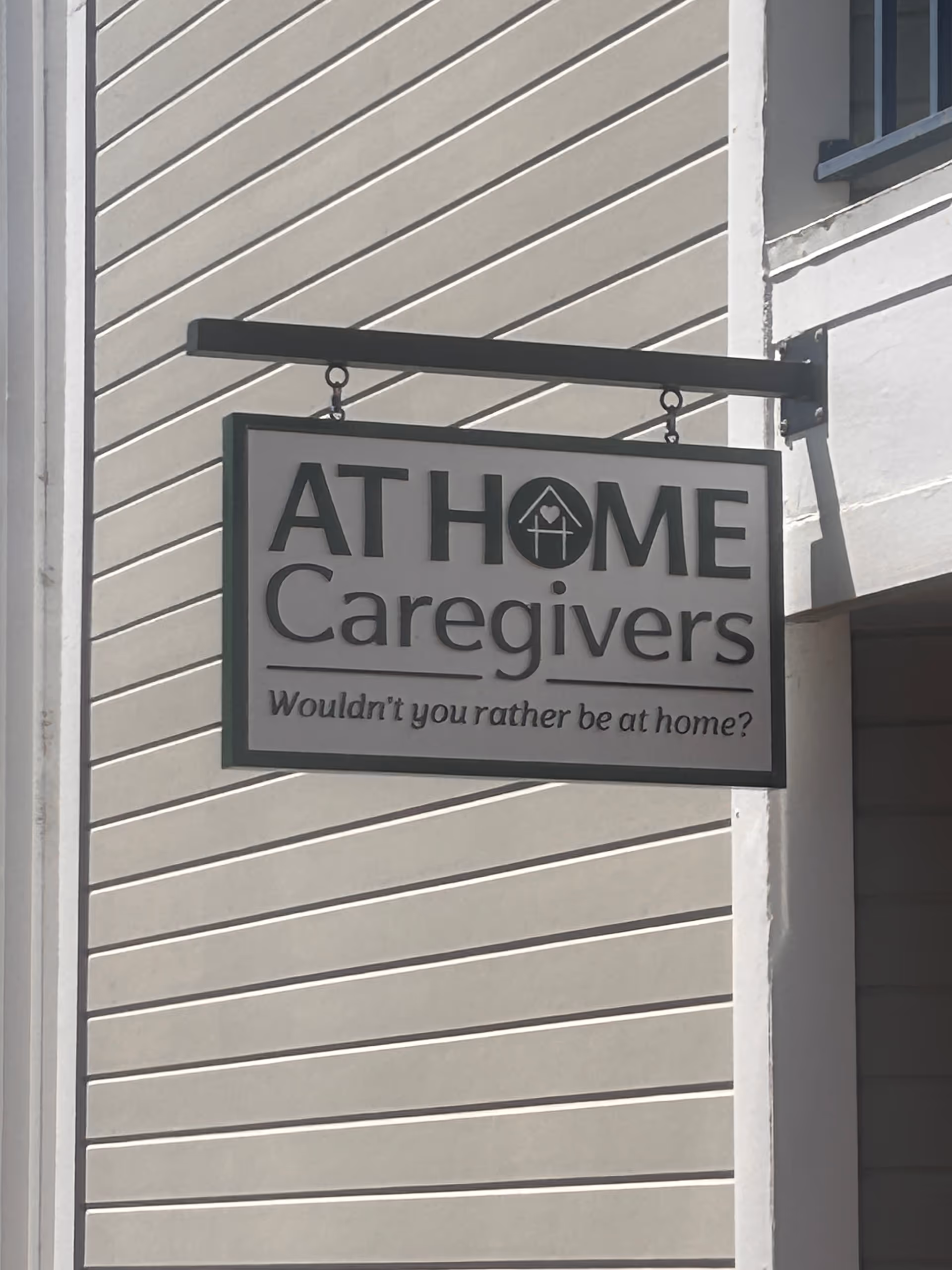 Exterior view of a building sign reading AT HOME Caregivers on siding.