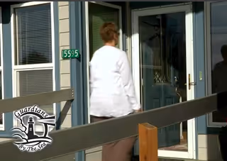 Individual in white coat walks toward glass doors of Guardians by the Sea facility.