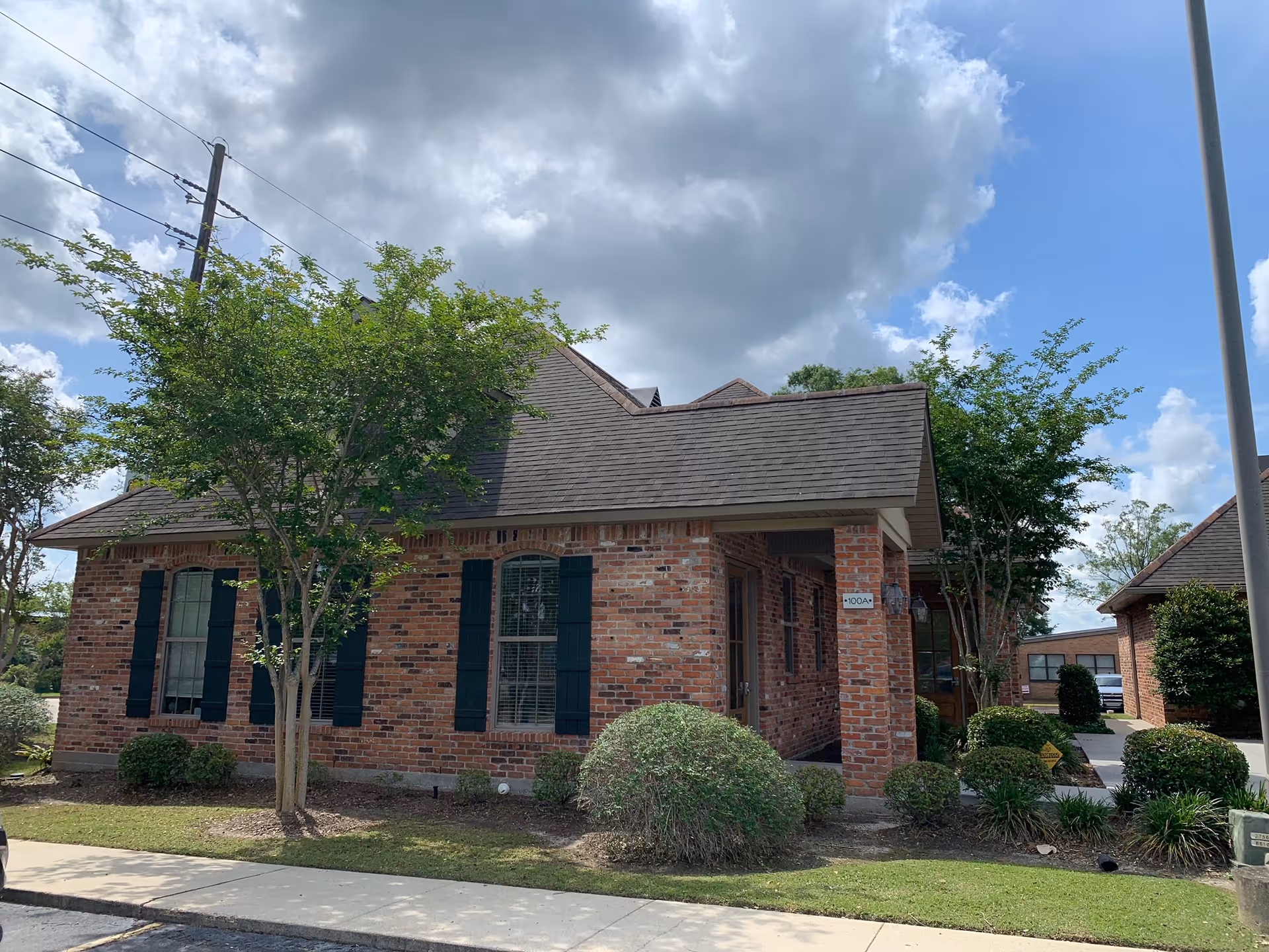 Brick, single-story facility exterior with green shutters, trees, and manicured shrubs.