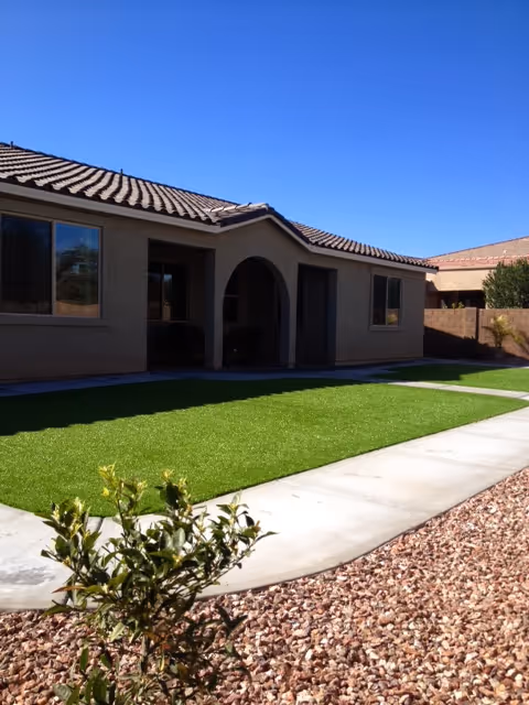 A single-story beige senior living building with an arched entrance, front lawn, and gravel landscaping.