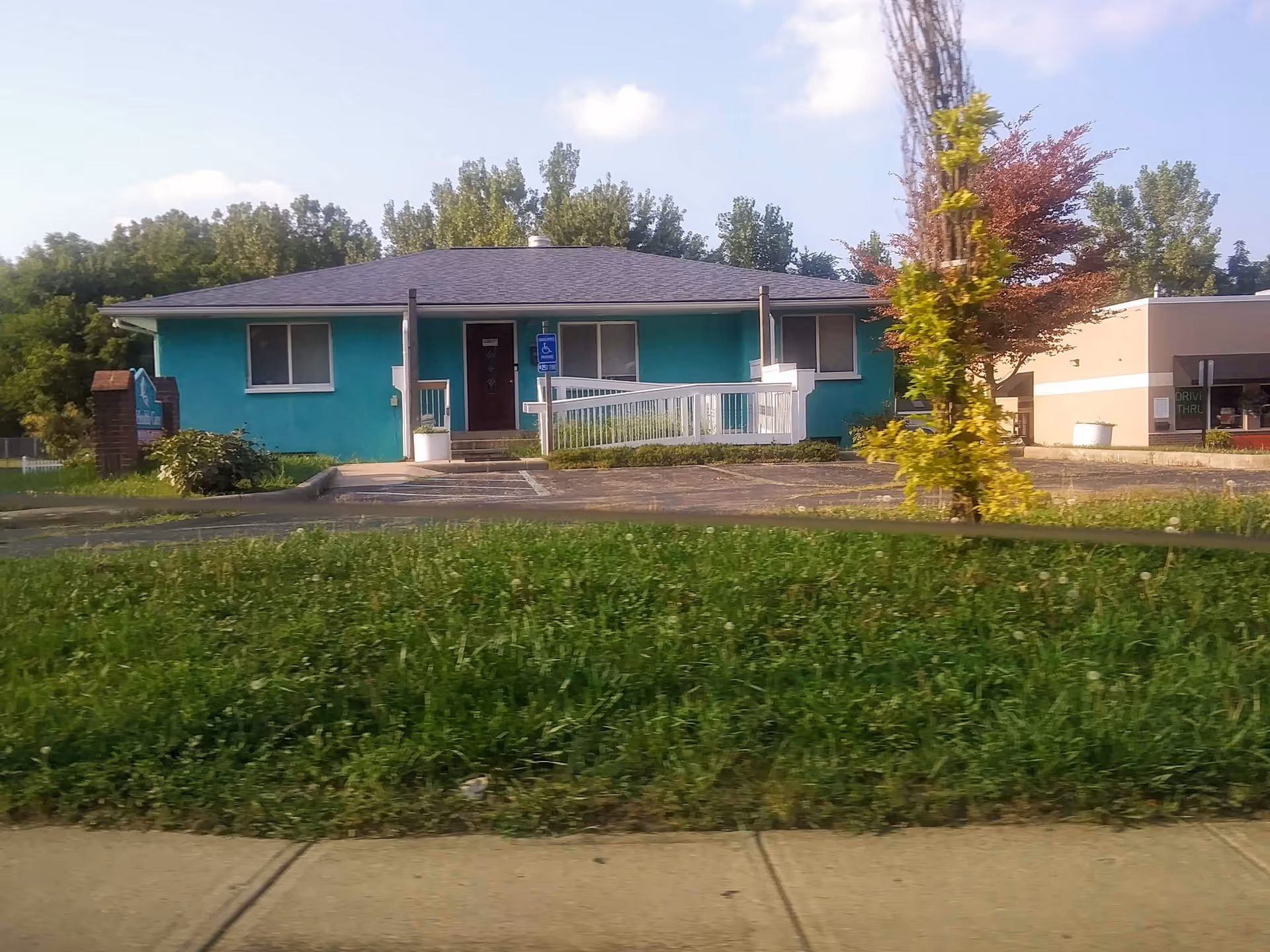 Exterior view of a teal, single-story senior care facility with a ramp