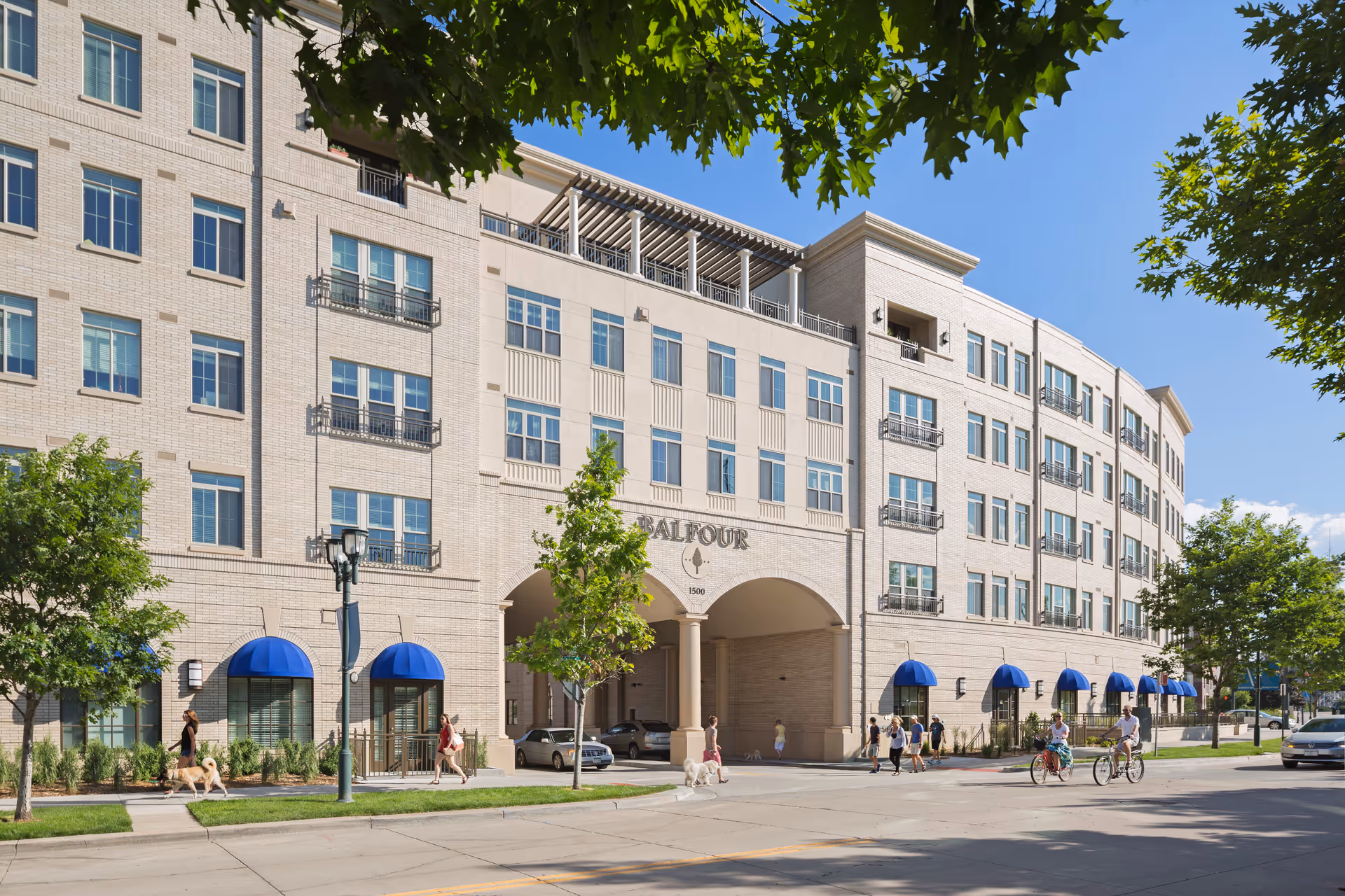 Beige multi-story senior living building (Balfour at Riverfront Park) with blue awnings and people.
