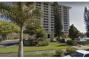 Tall residential building with a landscaped entrance and palm trees along a curved driveway.