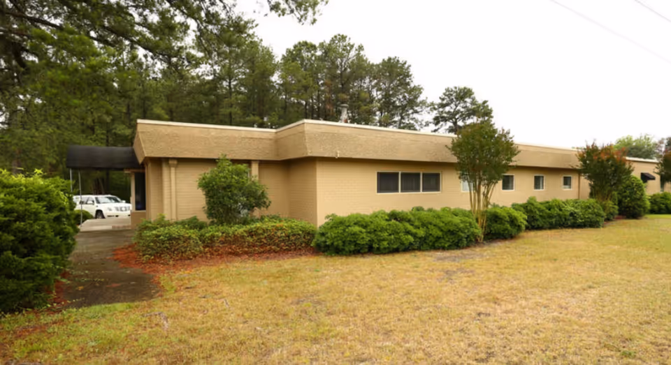 Exterior view of a beige facility with shrubs and a driveway entrance.