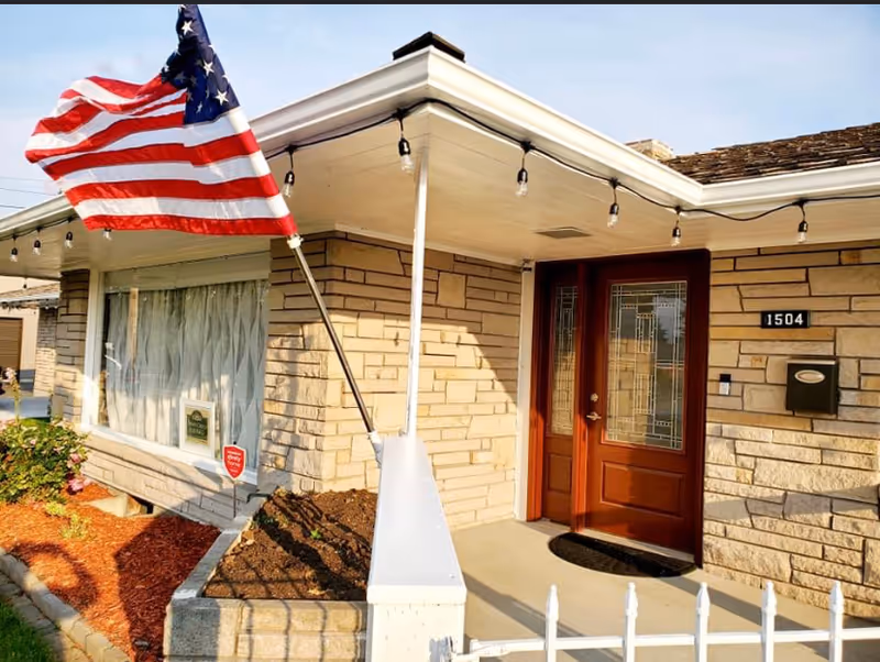 Front entrance of Compassionate Care Adult Family Home with American flag and stone facade.
