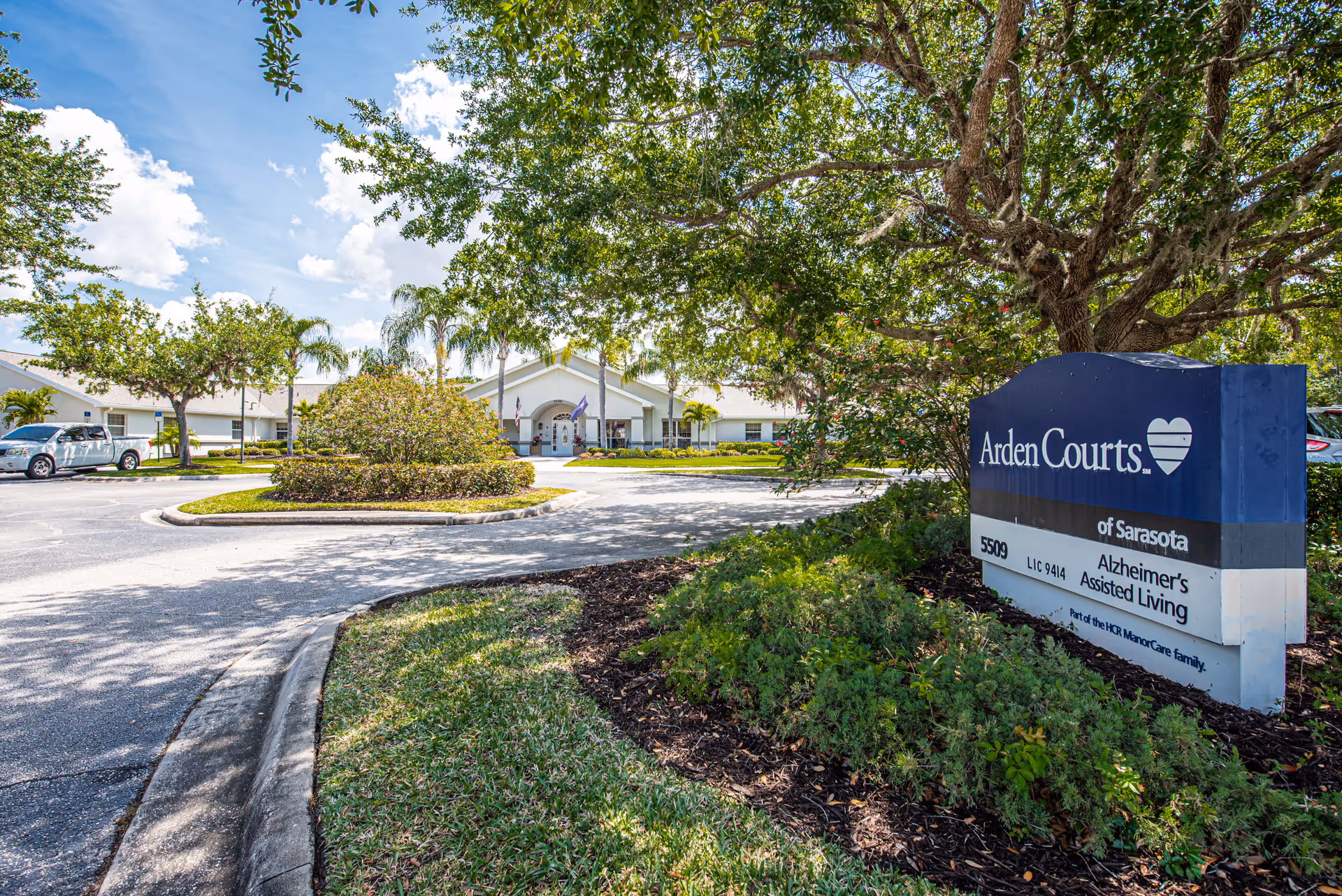 Front exterior of Arden Courts memory care community showing the entrance, circular driveway, landscaped grounds, and a large Arden Courts sign.