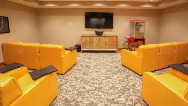 Small media room with yellow armchairs facing a wall-mounted TV and cabinet, with a popcorn machine in the corner.