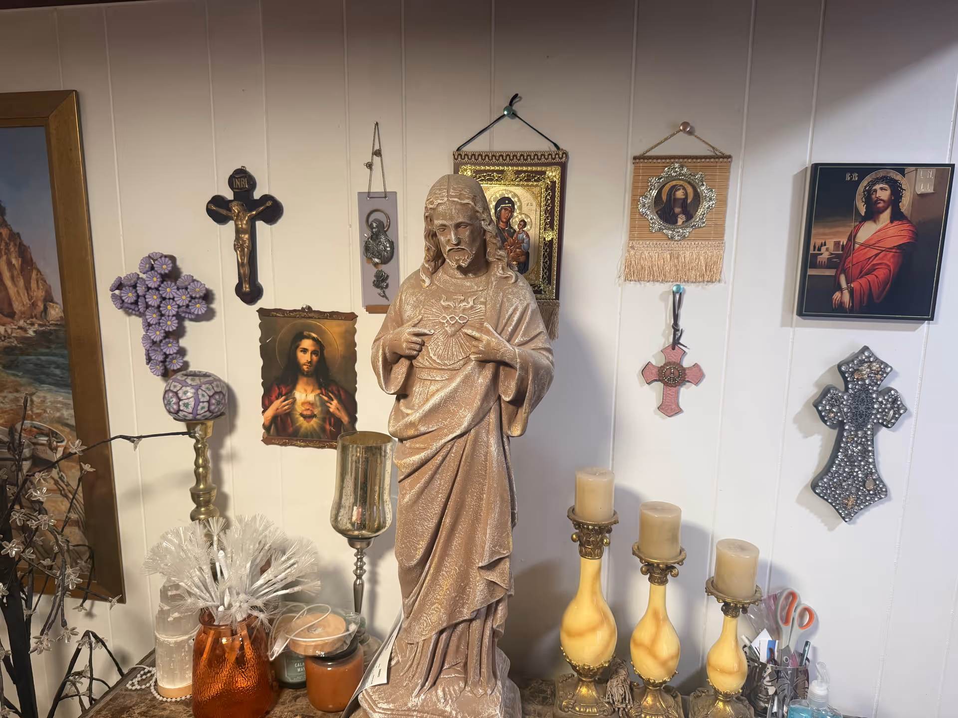 Religious shrine with statue, icons, and candles against a paneled wall.