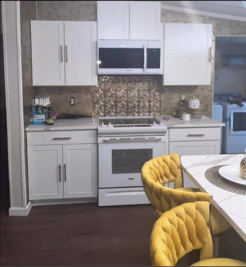 White kitchen with stove and microwave, tiled backsplash, and yellow upholstered dining chairs.