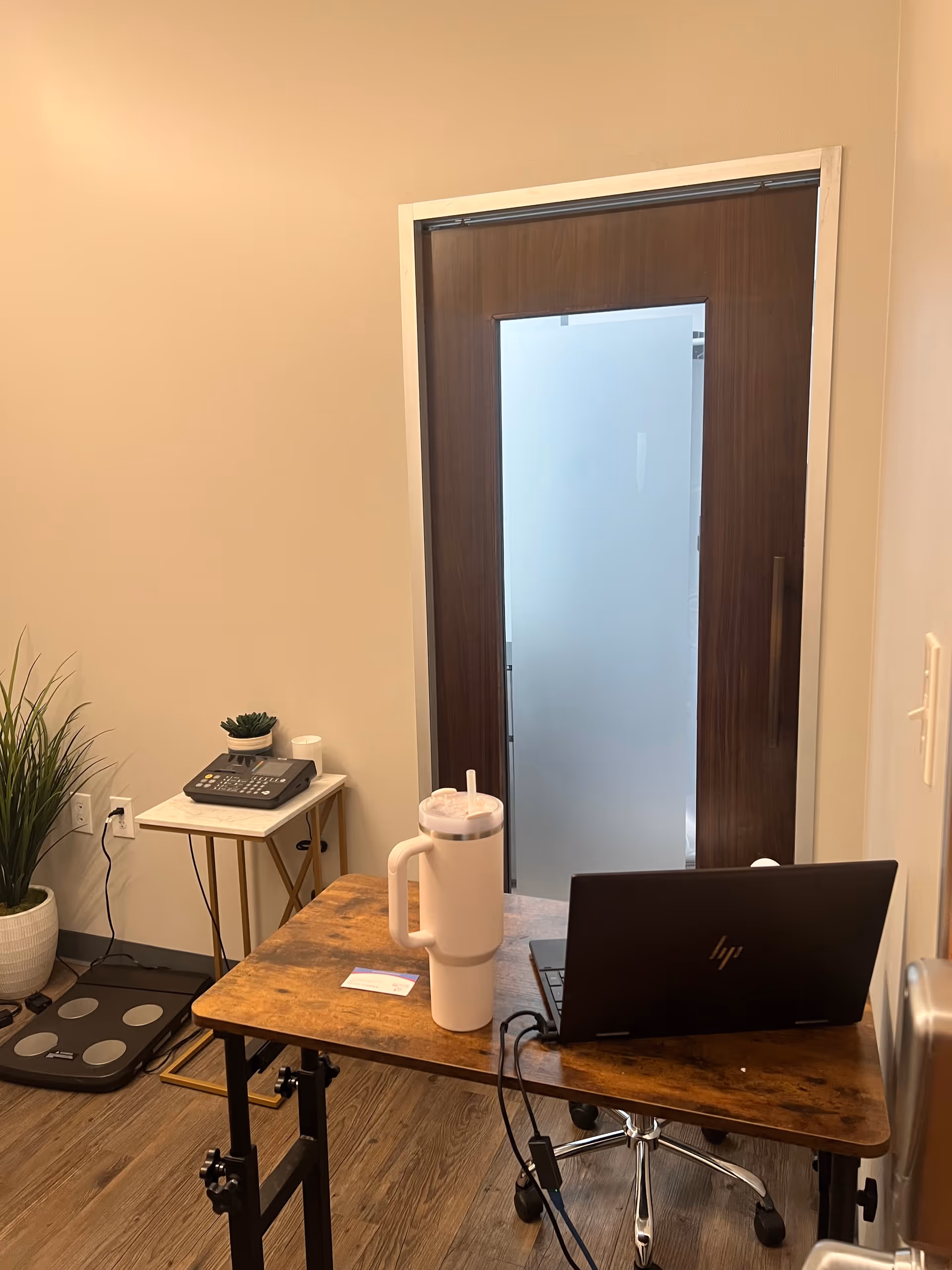 Small desk with a laptop and water bottle near a frosted glass door.
