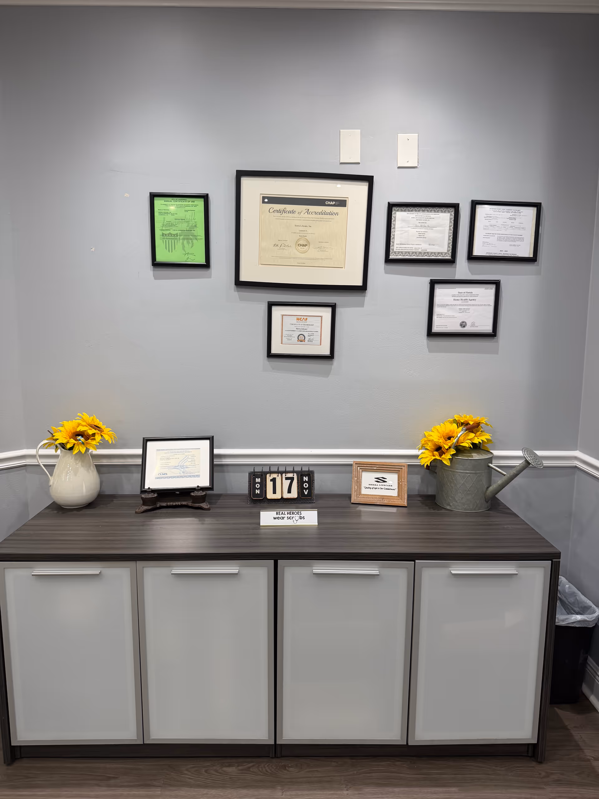 A reception-style counter with framed certificates on a gray wall and sunflowers.